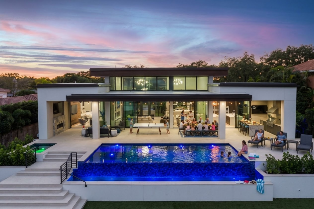 Tampa Bay luxury home built for entertaining: family dinner on a covered lanai with outdoor kitchen, open great room, and lit pool at dusk